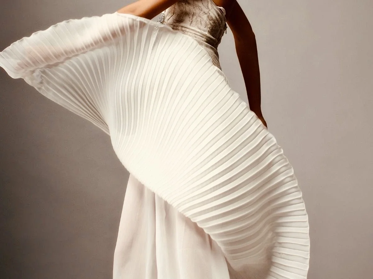 Woman in a flowing white pleated dress with arms raised in motion, symbolizing transformation, freedom, and stepping into the next version of yourself