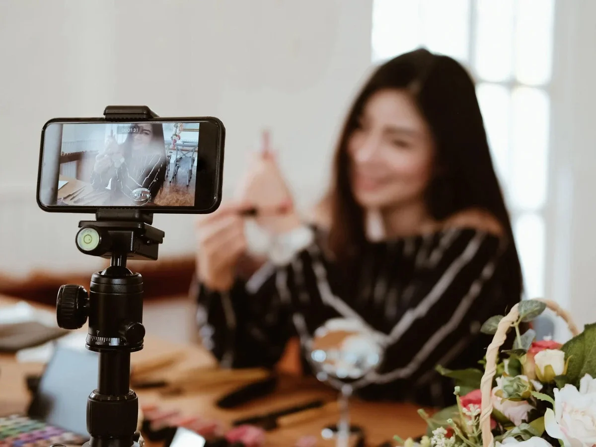 Woman filming herself on a phone mounted to a tripod, smiling for the camera
