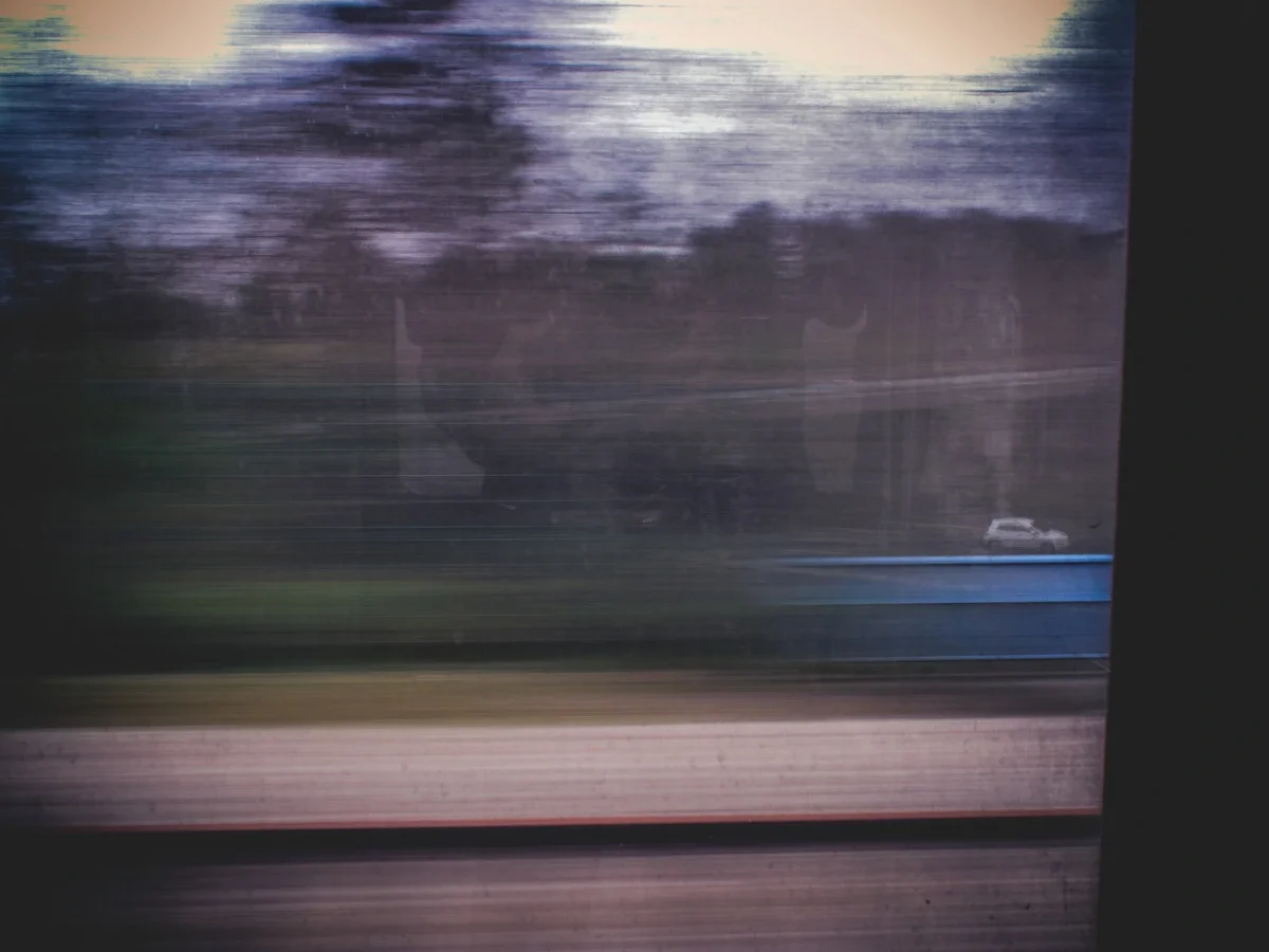Blurred train window with faint human reflection overlaid on a passing landscape at dusk