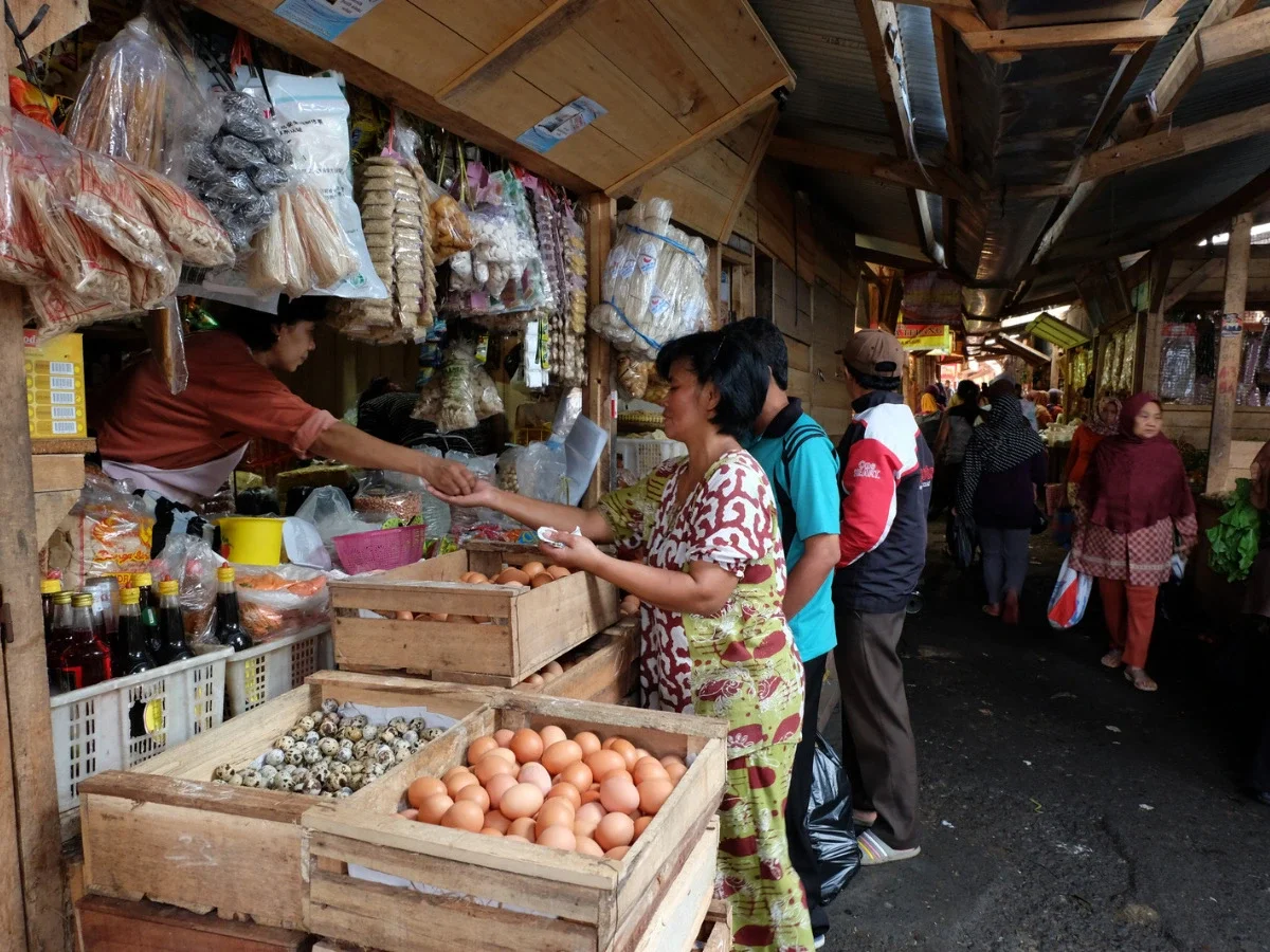 A vendor and customer exchanging goods hand to hand at an outdoor market stall