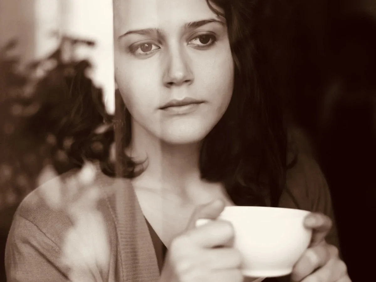 Contemplative woman holding a teacup gazing into the distance, illustrating the powerful link between scent, memory, and emotion
