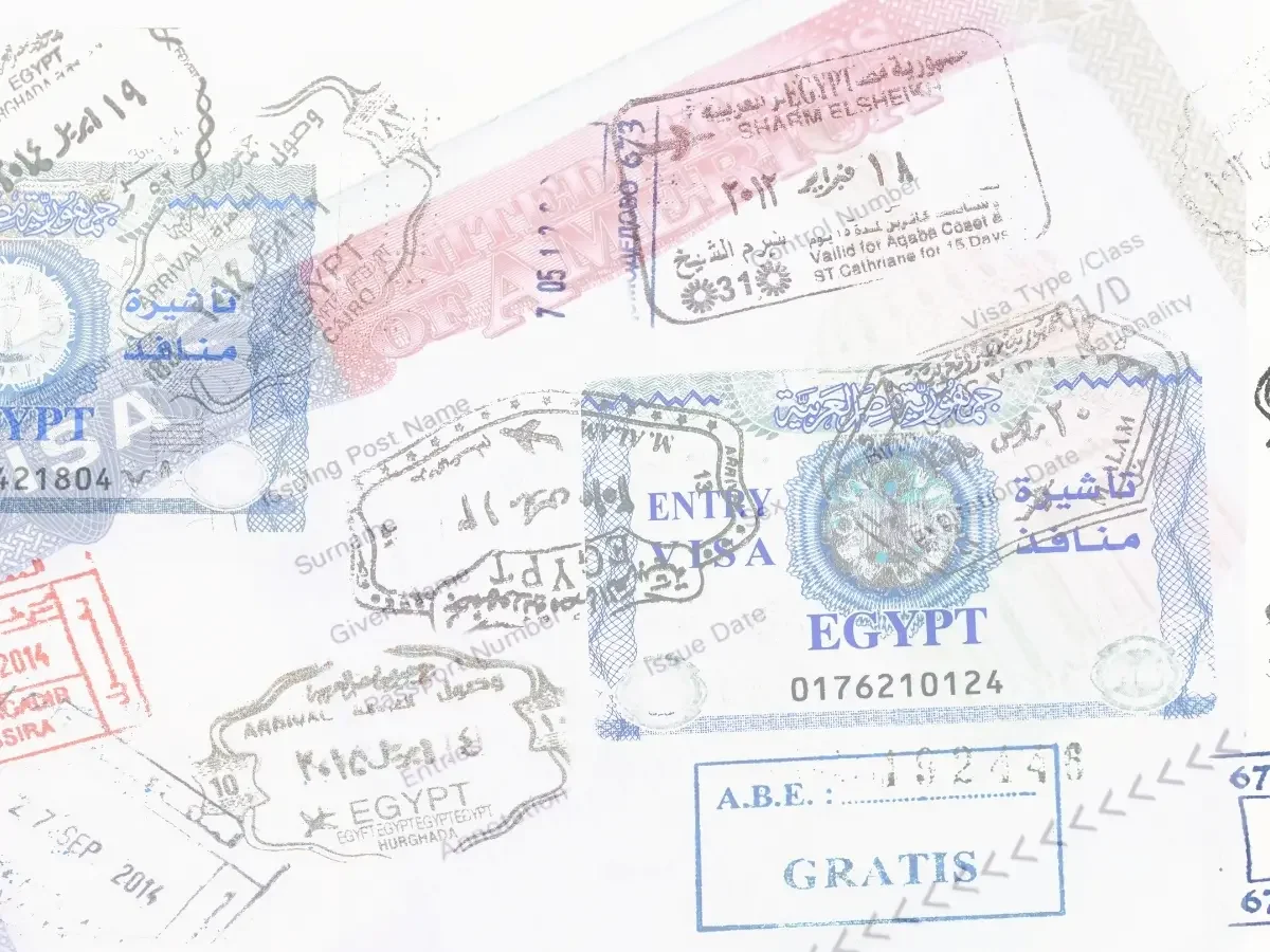 Overlapping passport stamps and entry visas from Egypt, layered across a well-traveled page — paired with archival letters to illustrate identity and reinvention in She The King's essay "When the Villain Feels Familiar."
