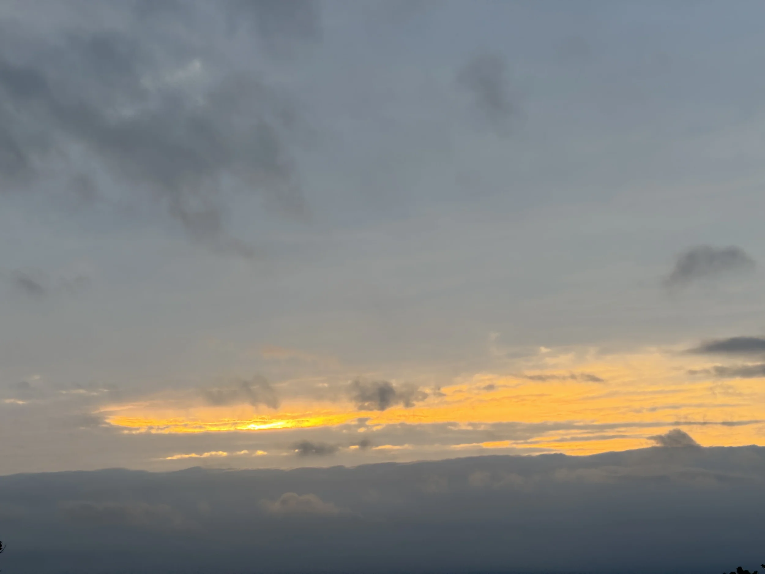 A narrow band of gold light breaking through layered gray clouds at dusk, evoking the stillness and patience of April Gornik's contemporary sky paintings.