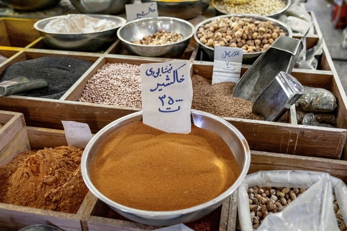 Bowls of Iranian spices, grains, and dried legumes in a traditional market, representing Persian culinary heritage and food as cultural storytelling in The Lion Women of Tehran.