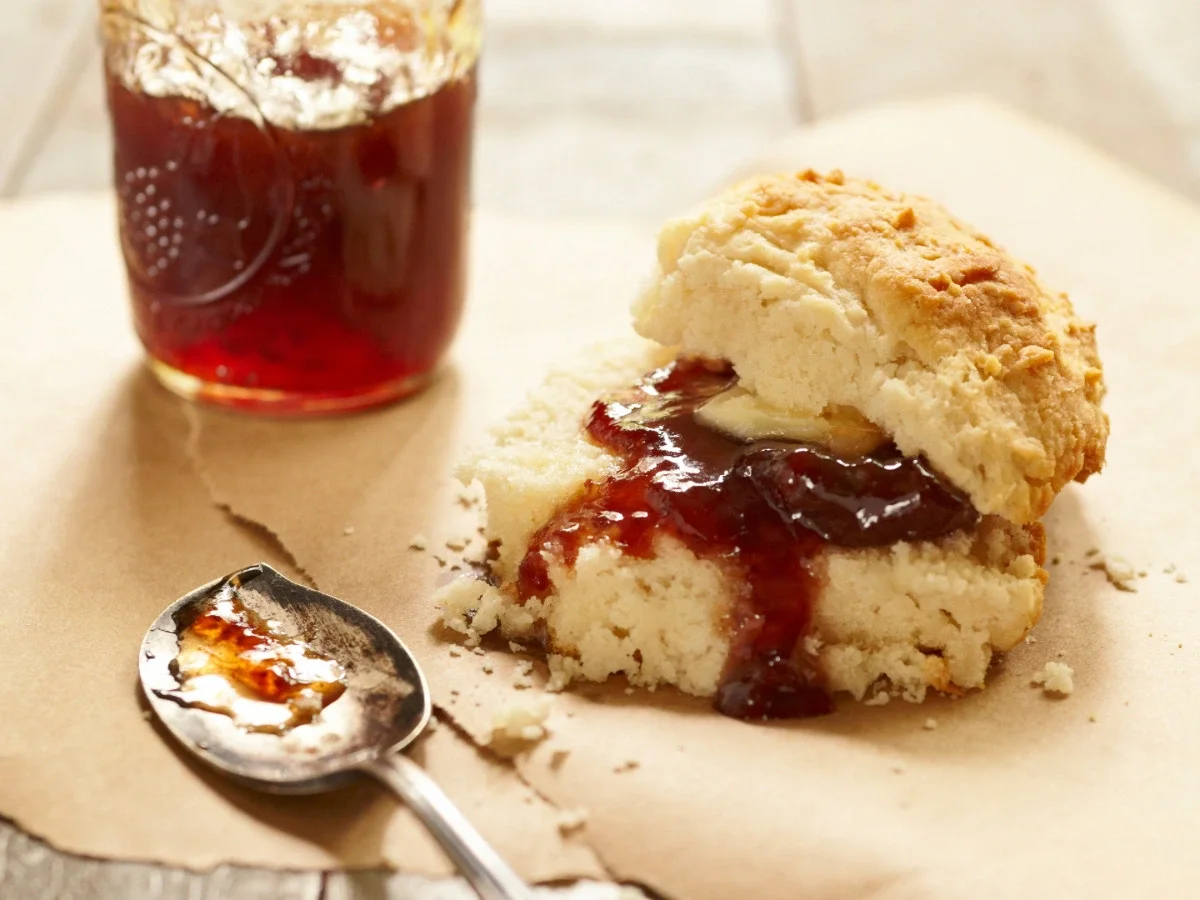 A split buttermilk biscuit filled with butter and jam on parchment paper—the tender pairing for Jamie in The Women