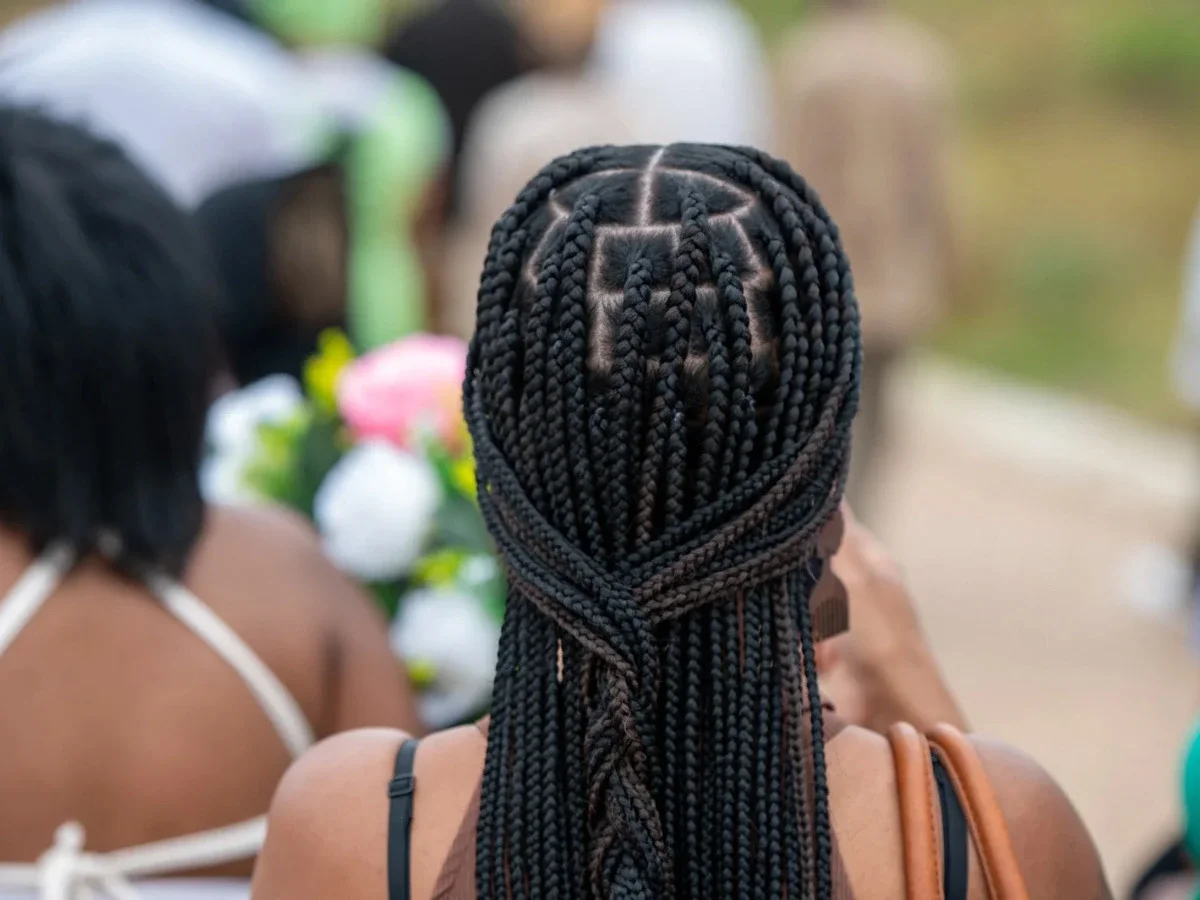 Back view of an intricately parted box braid style at an outdoor gathering, showing braiding as a visual language and cultural craft