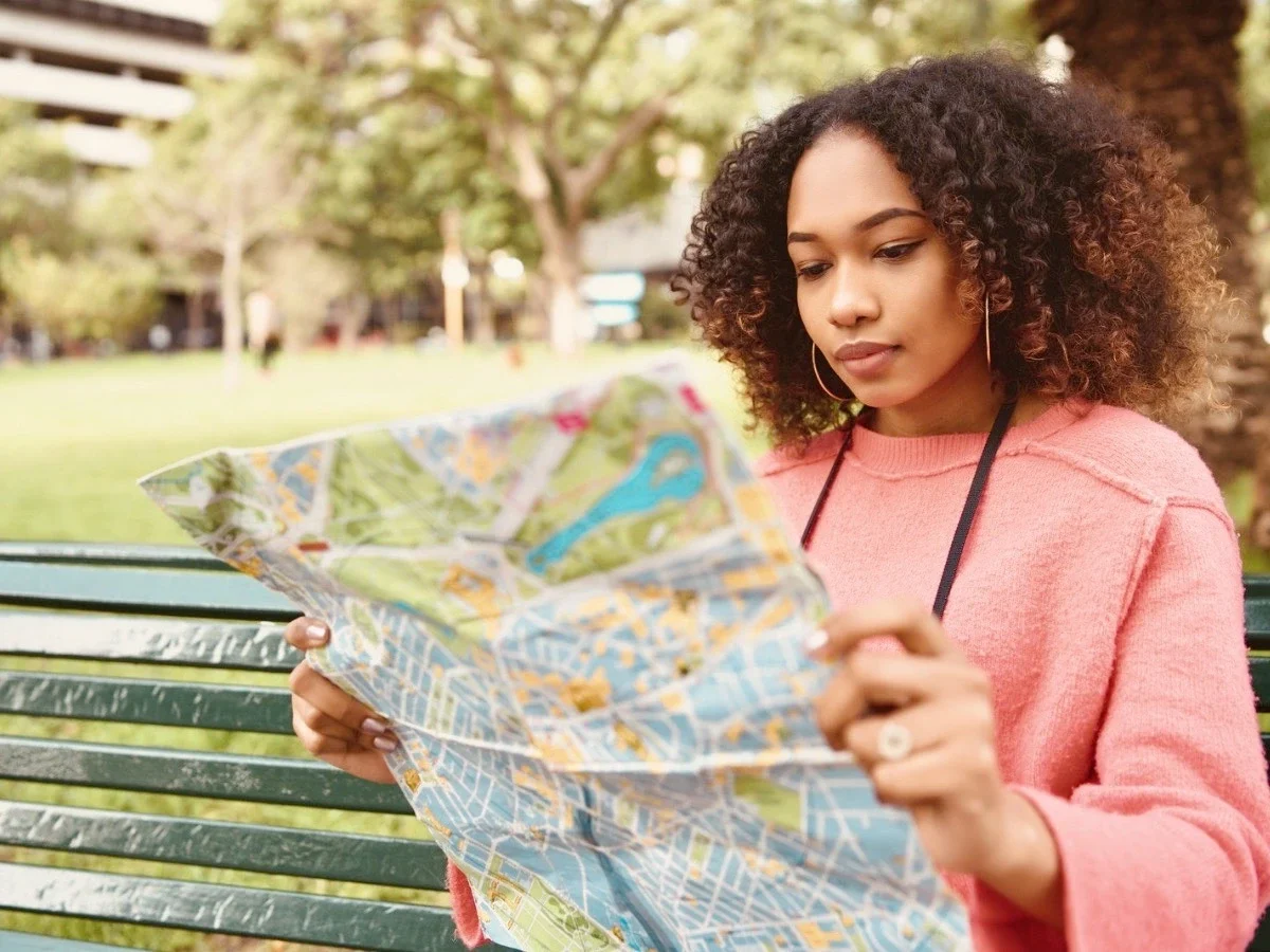 A woman with curly hair studying a city map while seated on a park bench