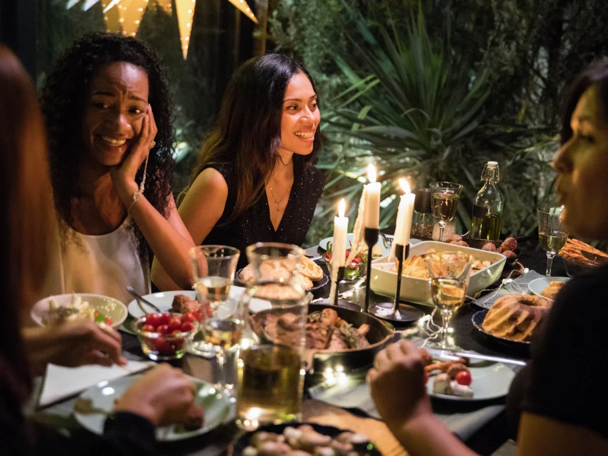 Friends gathered around a candlelit outdoor dinner table during a warm summer evening conversation.