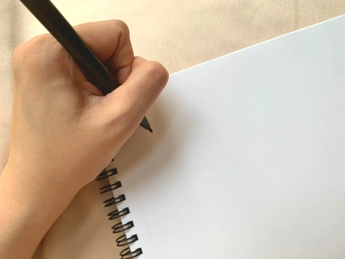 An open notebook with a blank page and a pen poised to write, symbolizing the unfinished nature of becoming