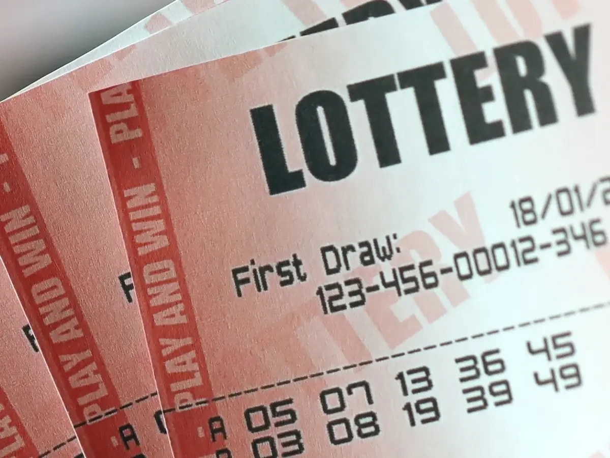 : A hand holding fanned lottery tickets over a blurred play slip, an image of the one thing a family leaves behind.