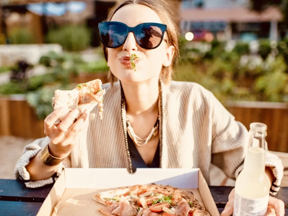 A woman dining alone outdoors, eating pizza and enjoying herself in the sunshine