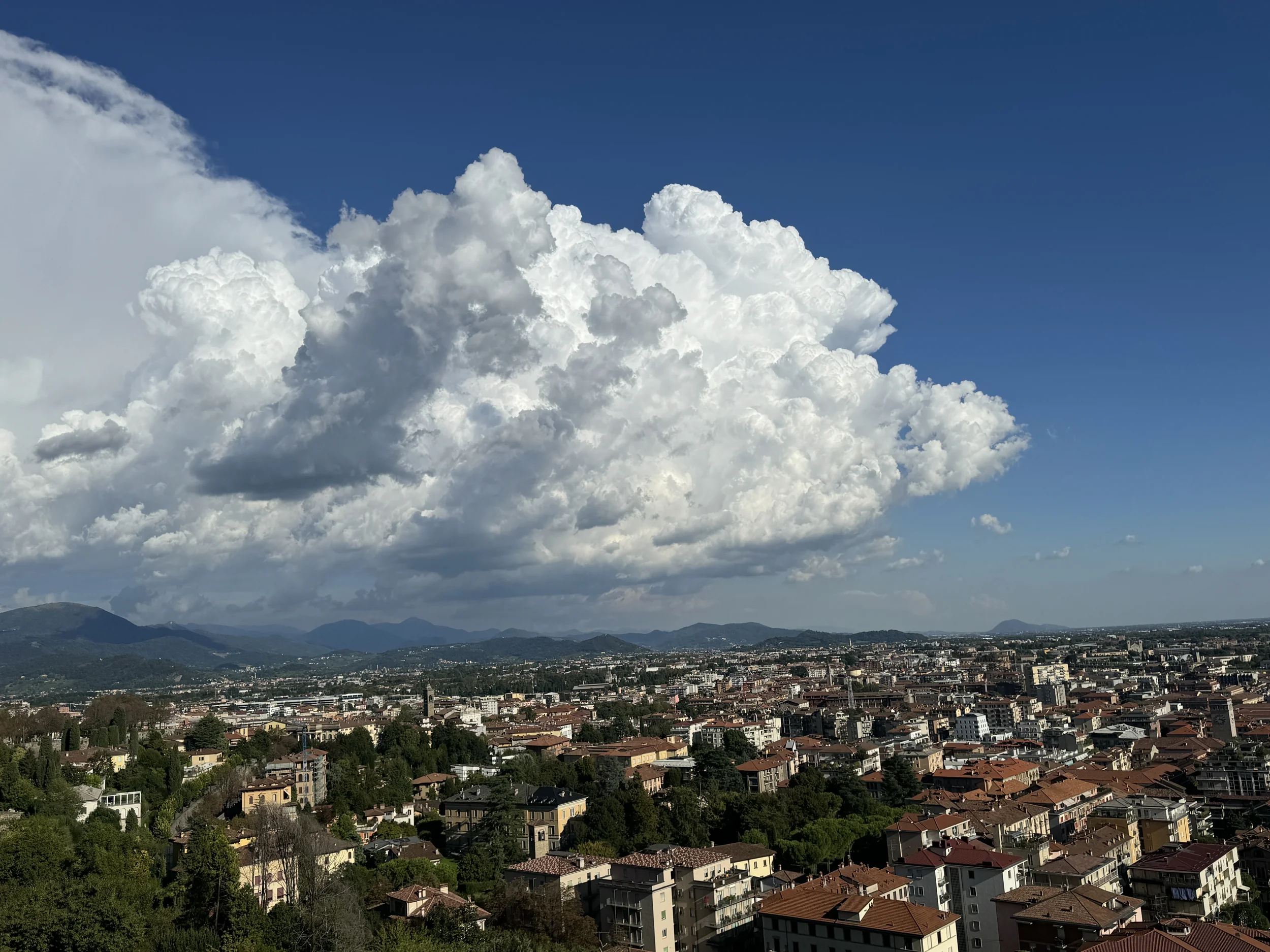A towering cumulus cloud dominates the sky above a European hillside town, illustrating the vast scale of sky landscape painters like Ruisdael captured on canvas.