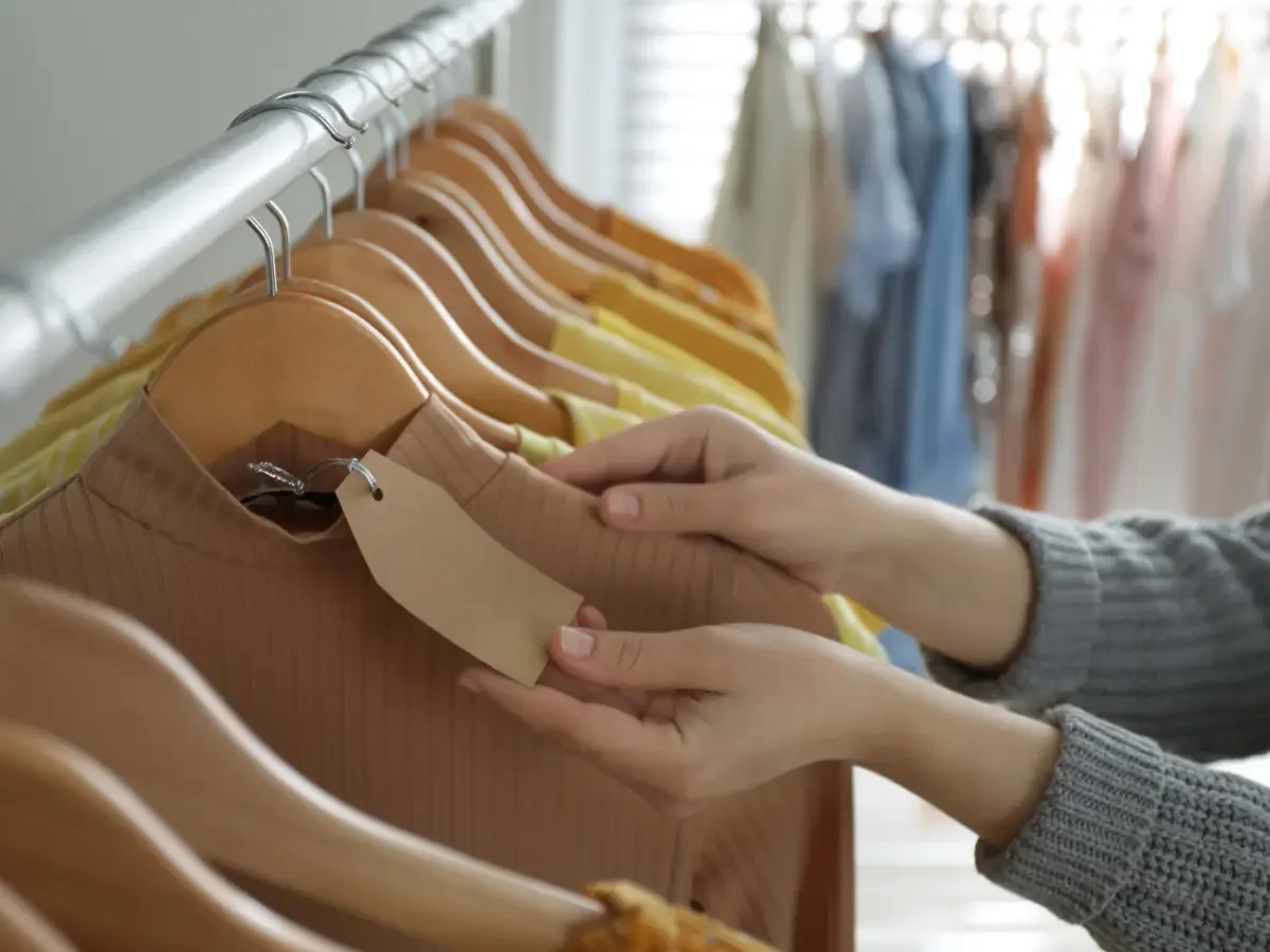 Two hands holding a blank paper tag on a ribbed top in a clothing rack, suggesting how families measure the people they love.