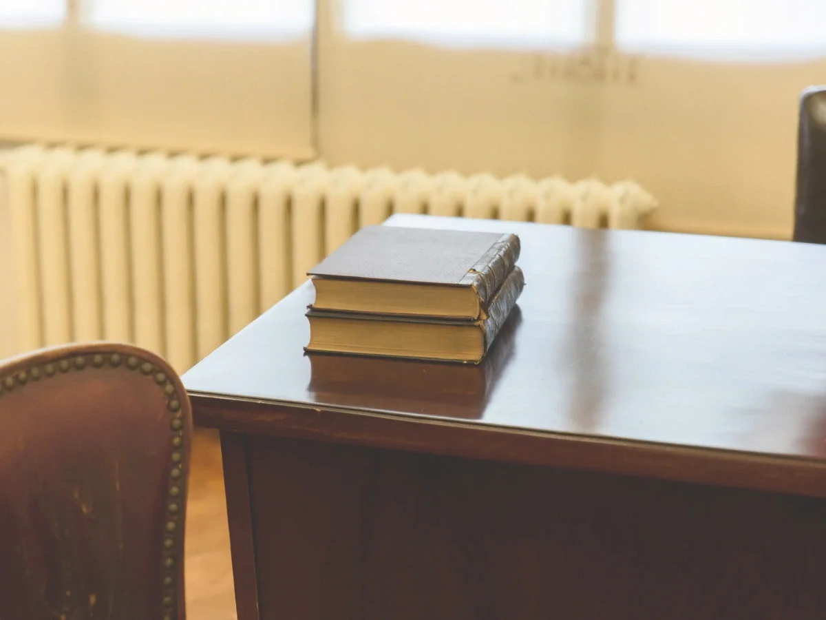 A plain wooden desk and bench beneath a bare window looking out on winter branches, shot in sepia tone — accompanying "What You'd Want, Unexplained," on She The King's essay about naming small, undramatic desires.