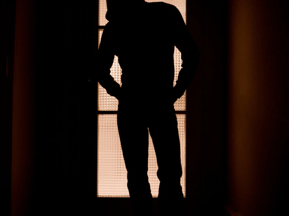 Silhouette of a man standing still in a backlit doorway with frosted glass panels