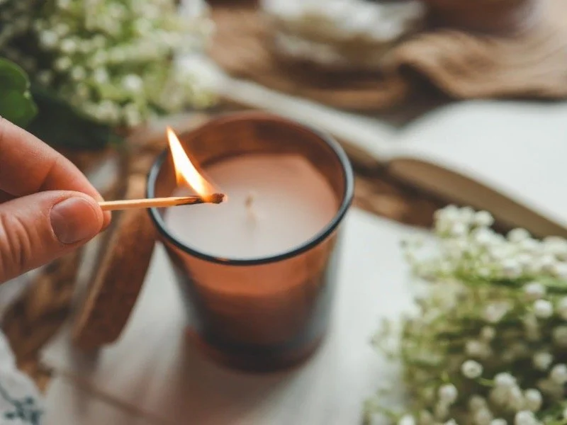 Hand lighting a candle in a calming, cozy setting, symbolizing inner and outer self-care and the nourishing micro-habits for a softer 2026.