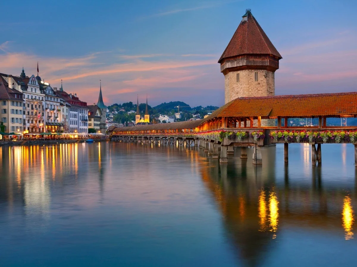 Kapellbrücke (Chapel Bridge) crossing the Reuss River in Lucerne at sunset with reflections on the water.