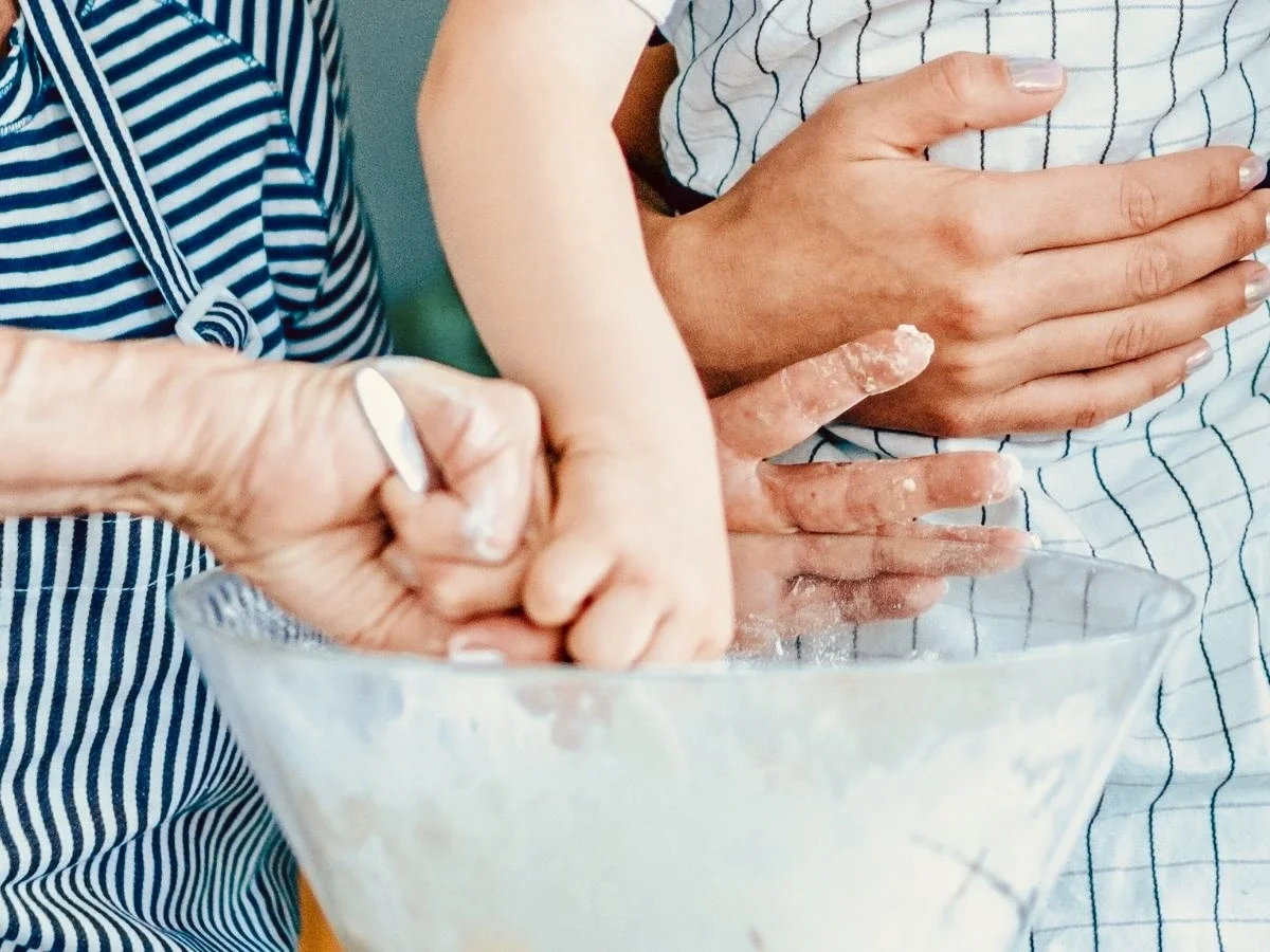 Child's and adult's hands mixing flour in a glass bowl during a shared cooking lesson