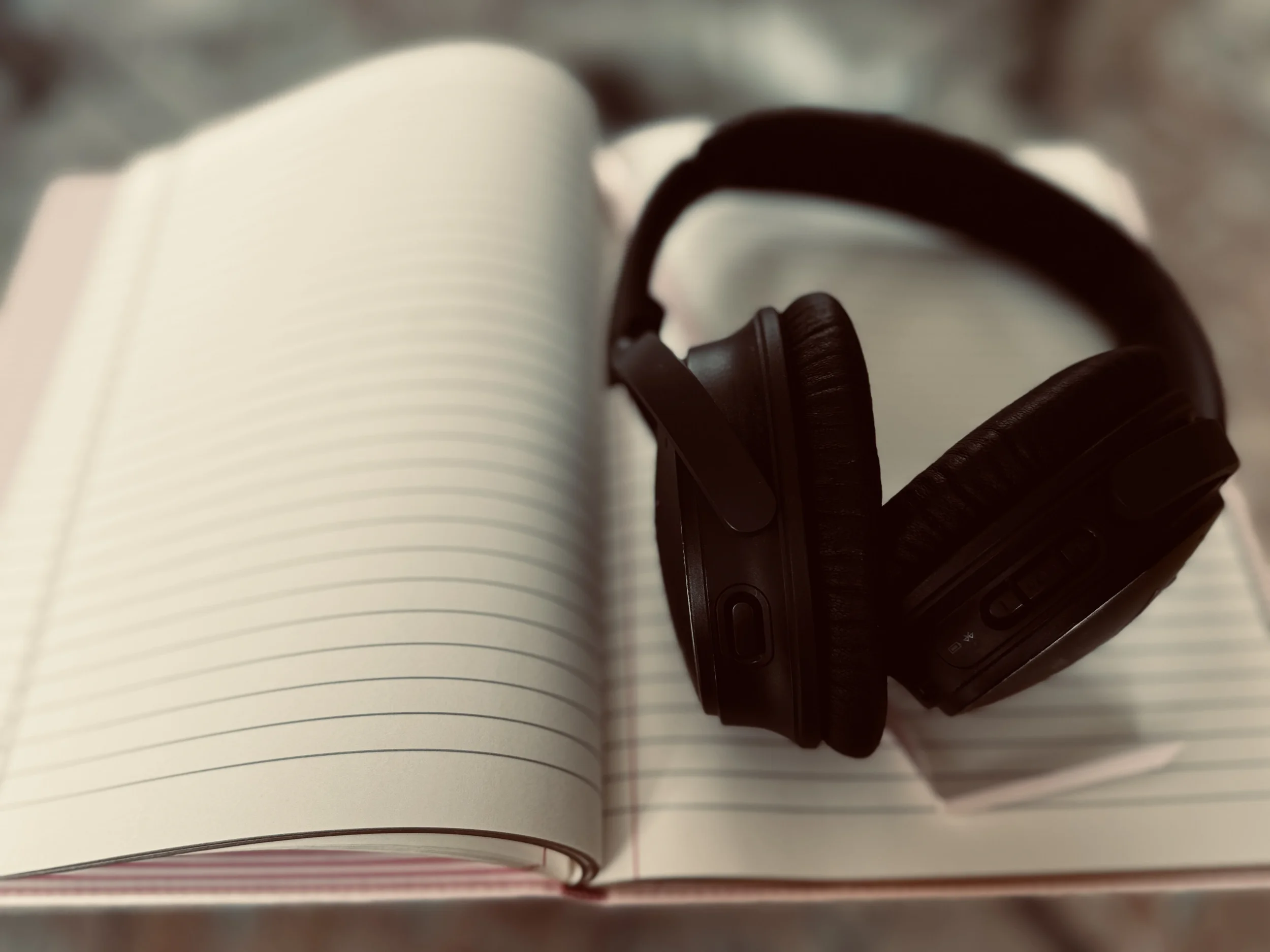 A pair of black over-ear headphones resting on the open pages of a lined notebook, photographed in muted tones.