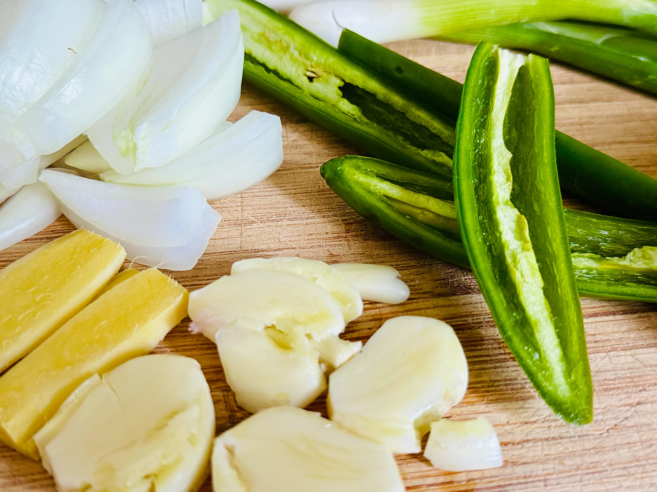 Close-up of jangjorim preparation ingredients on a wooden cutting board including sliced ginger, crushed garlic cloves, onion wedges, and halved green peppers