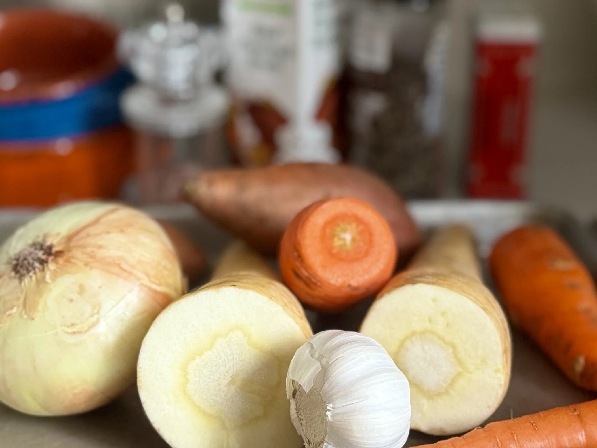 Fresh root vegetables for roasted soup — onion, parsnip, carrots, sweet potato, and garlic arranged on a kitchen counter, ingredients for the Wild Dark Shore food pairing recipe.