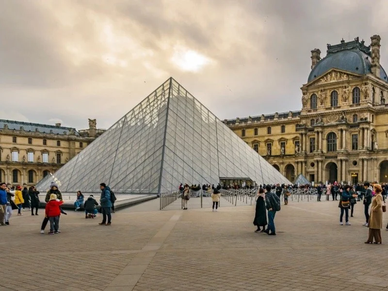 Crowds gathered around the glass pyramid at the Louvre Museum in Paris, showcasing iconic architecture that inspires museum-themed art and wellness gifts.
