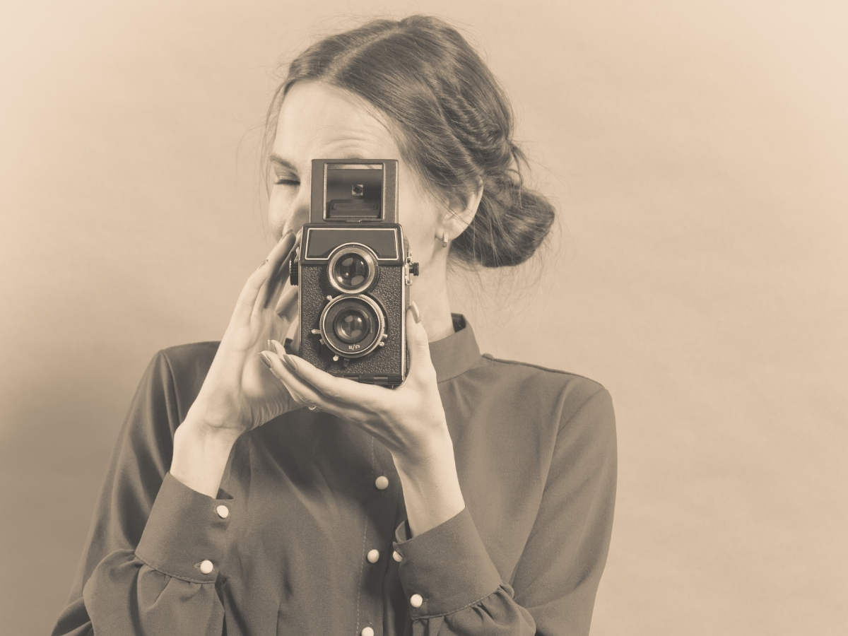Sepia-toned portrait of a woman looking down into a vintage twin-lens reflex camera to compose a shot