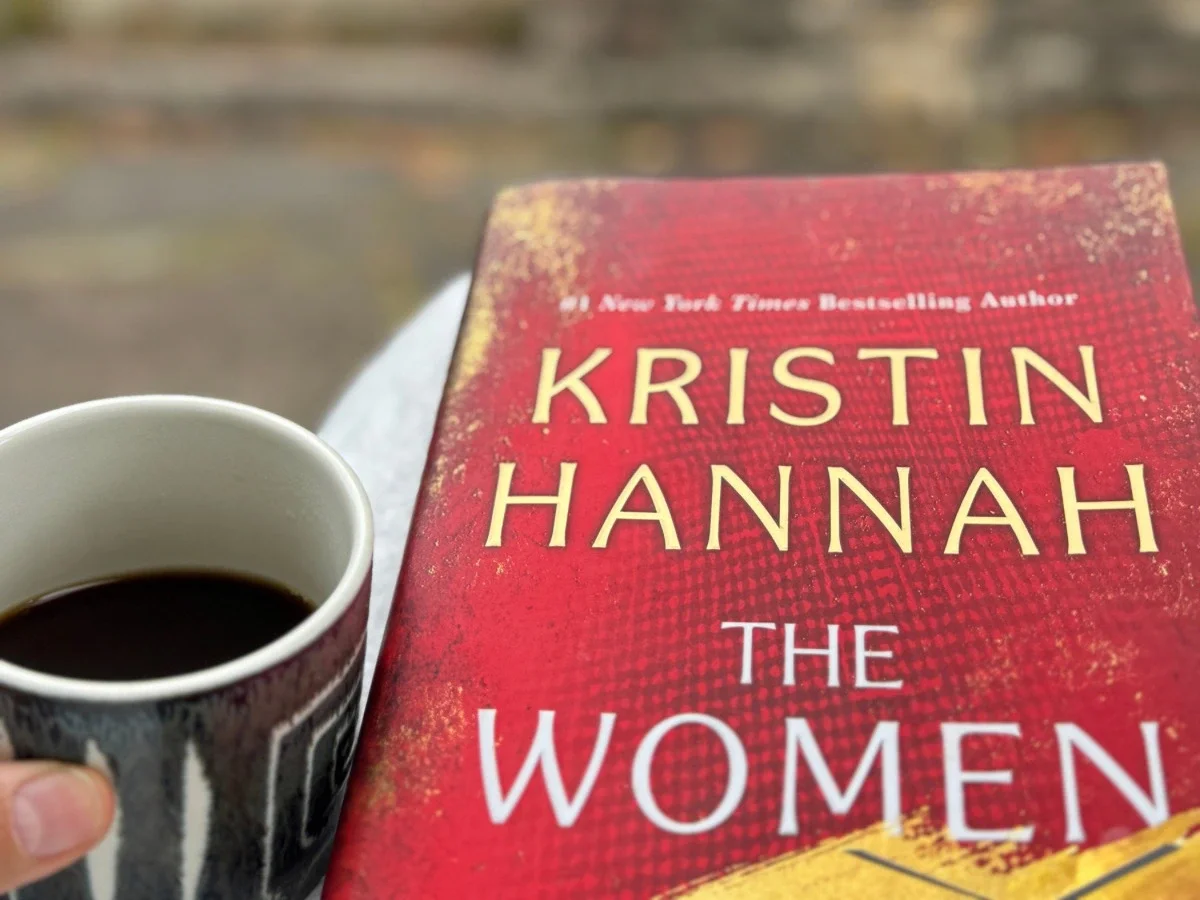 Copy of The Women by Kristin Hannah with a cup of coffee, August book pick review on shetheking.com