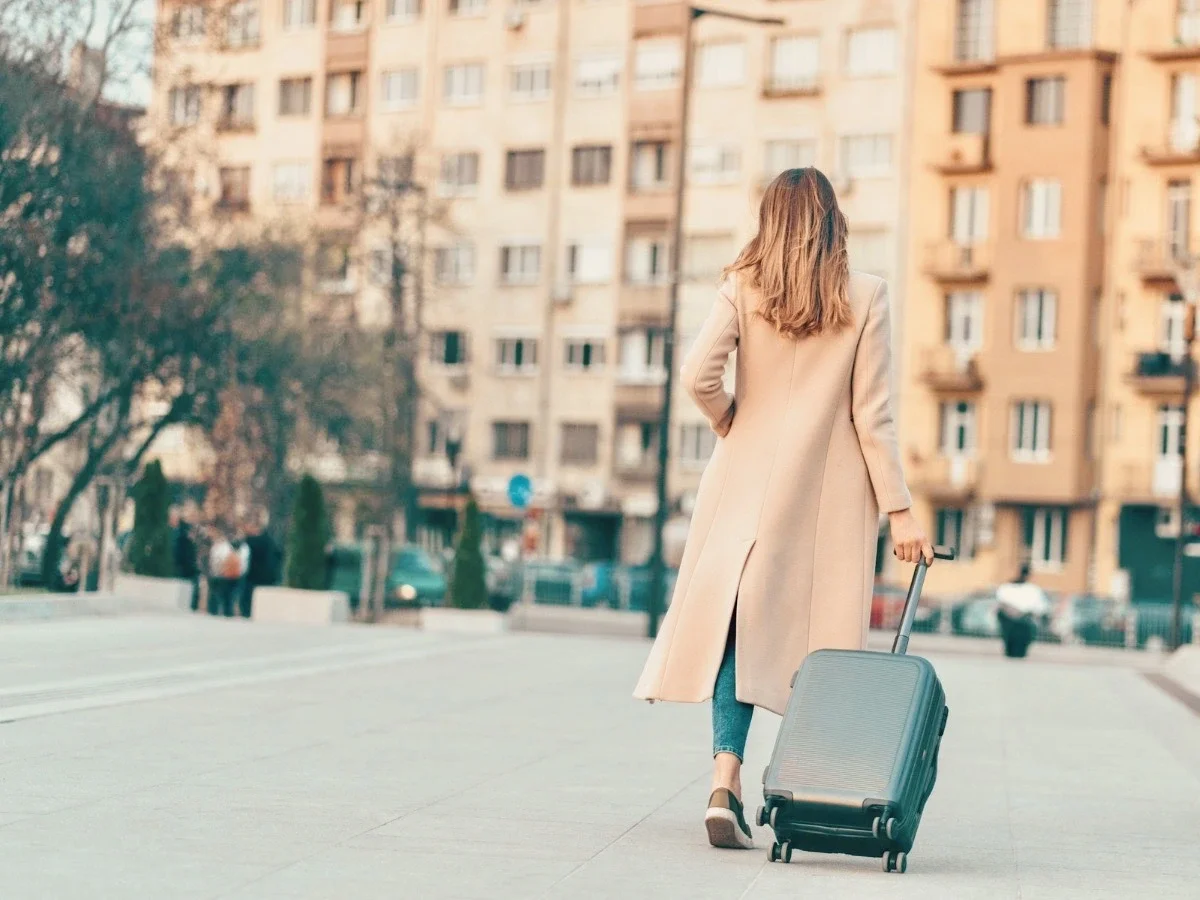 A woman in a beige coat pulling a suitcase alone through a European city street