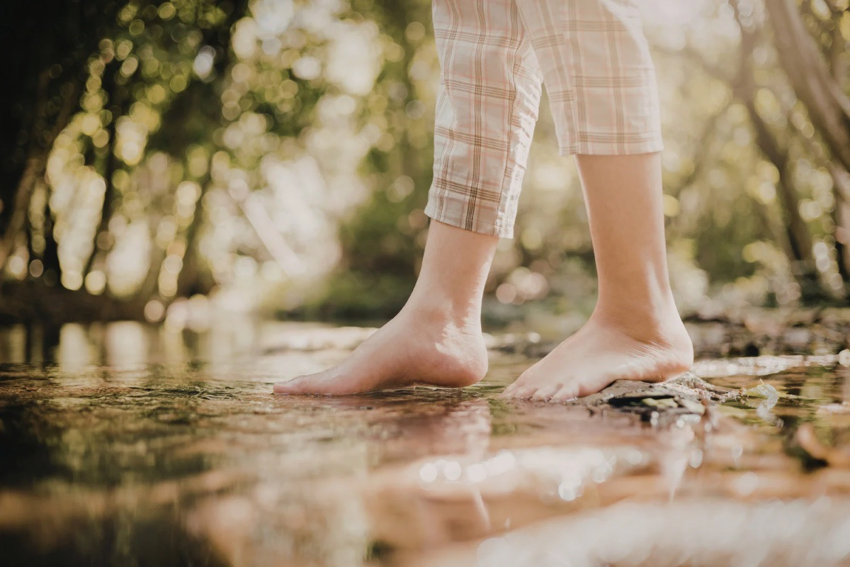 Close-up of feet in a shallow stream, symbolizing grounding, presence, and reconnecting with nature as part of a calming spring reset and intentional lifestyle.