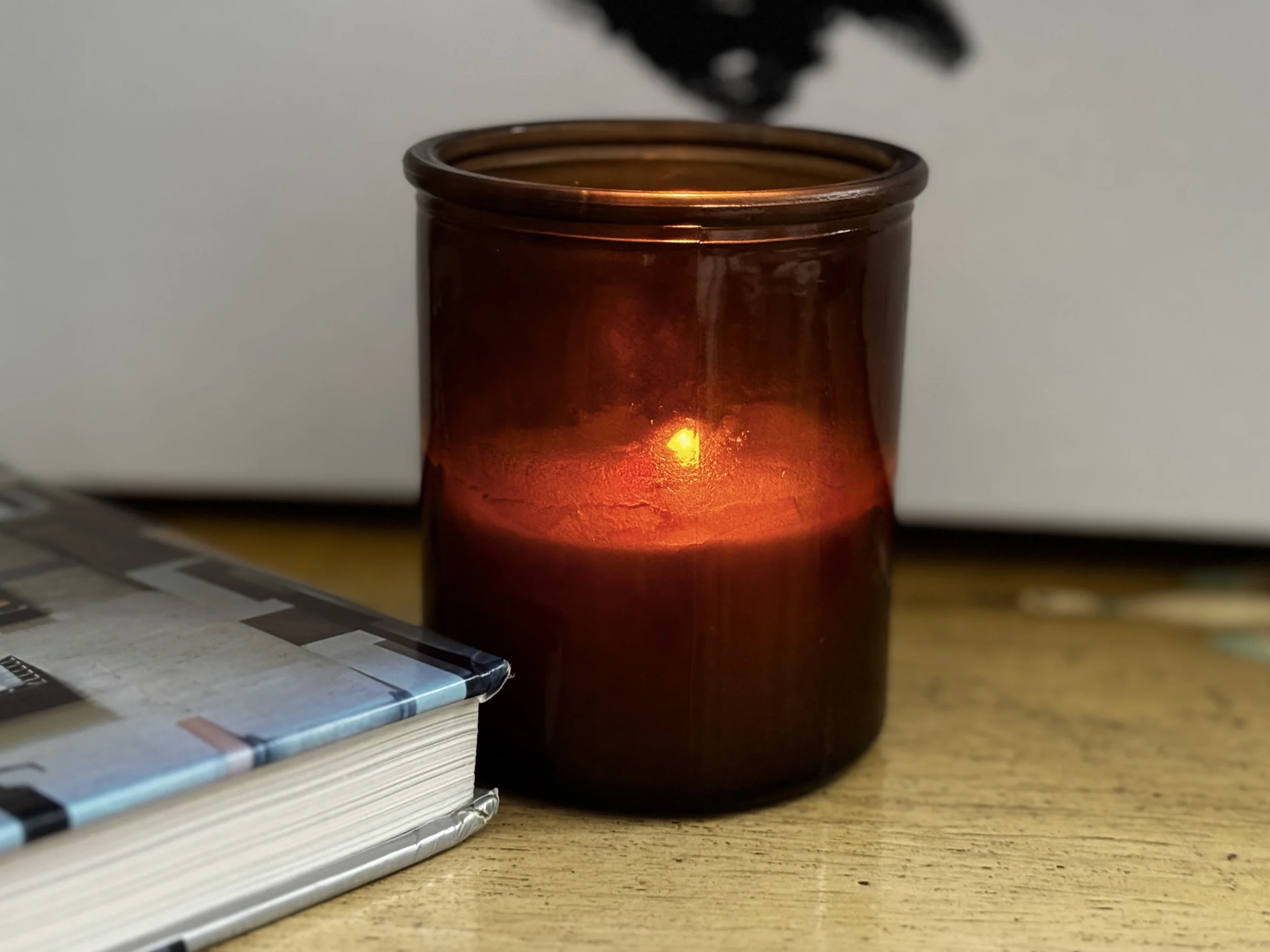 An open art book on a wooden surface with a lit candle glowing softly behind it — the solitary, intimate experience of turning to art in grief