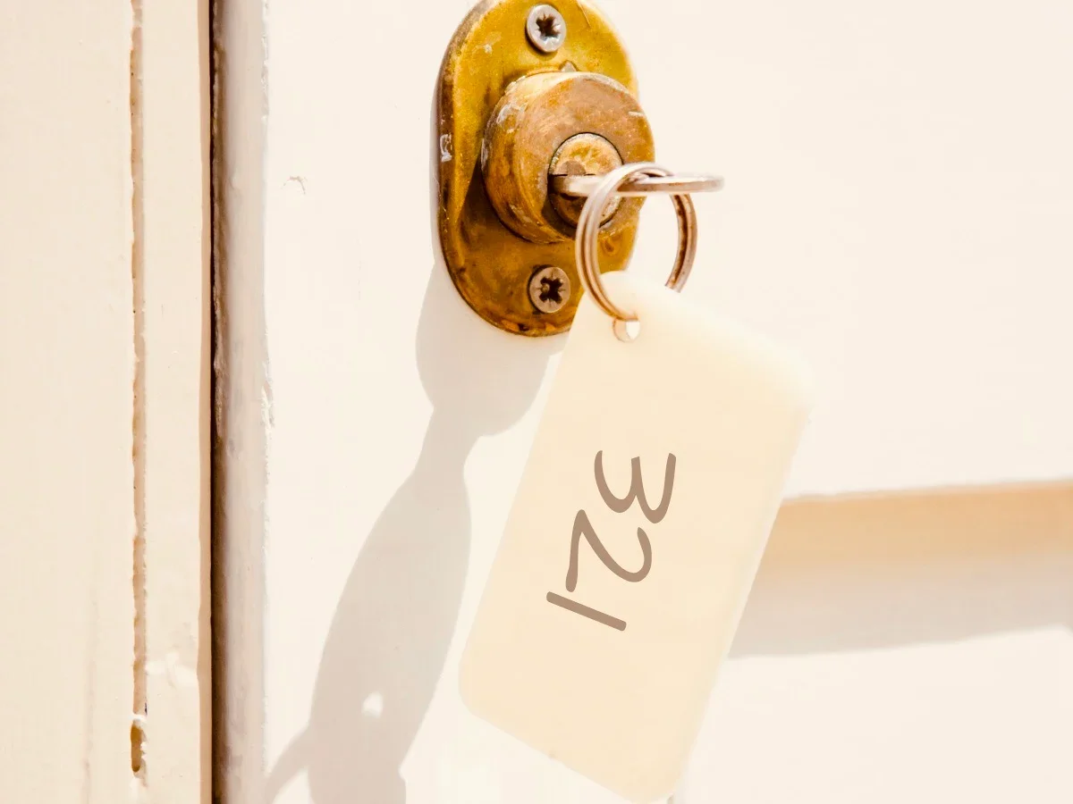 Vintage motel room key with number tag left in a brass door lock, soft daylight on a white painted door