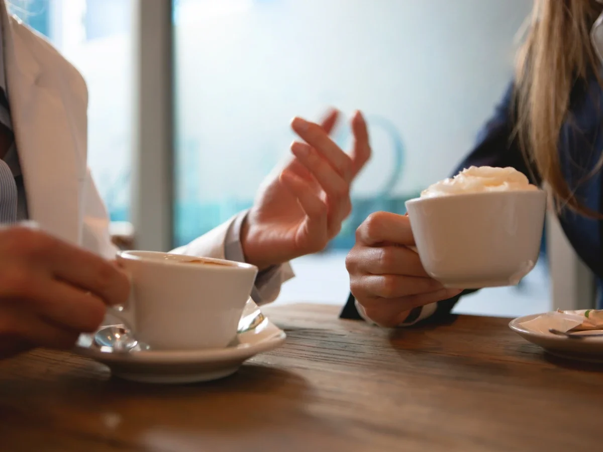 Close-up of hands mid-gesture over coffee cups during conversation, evoking the effort of communicating across a language gap