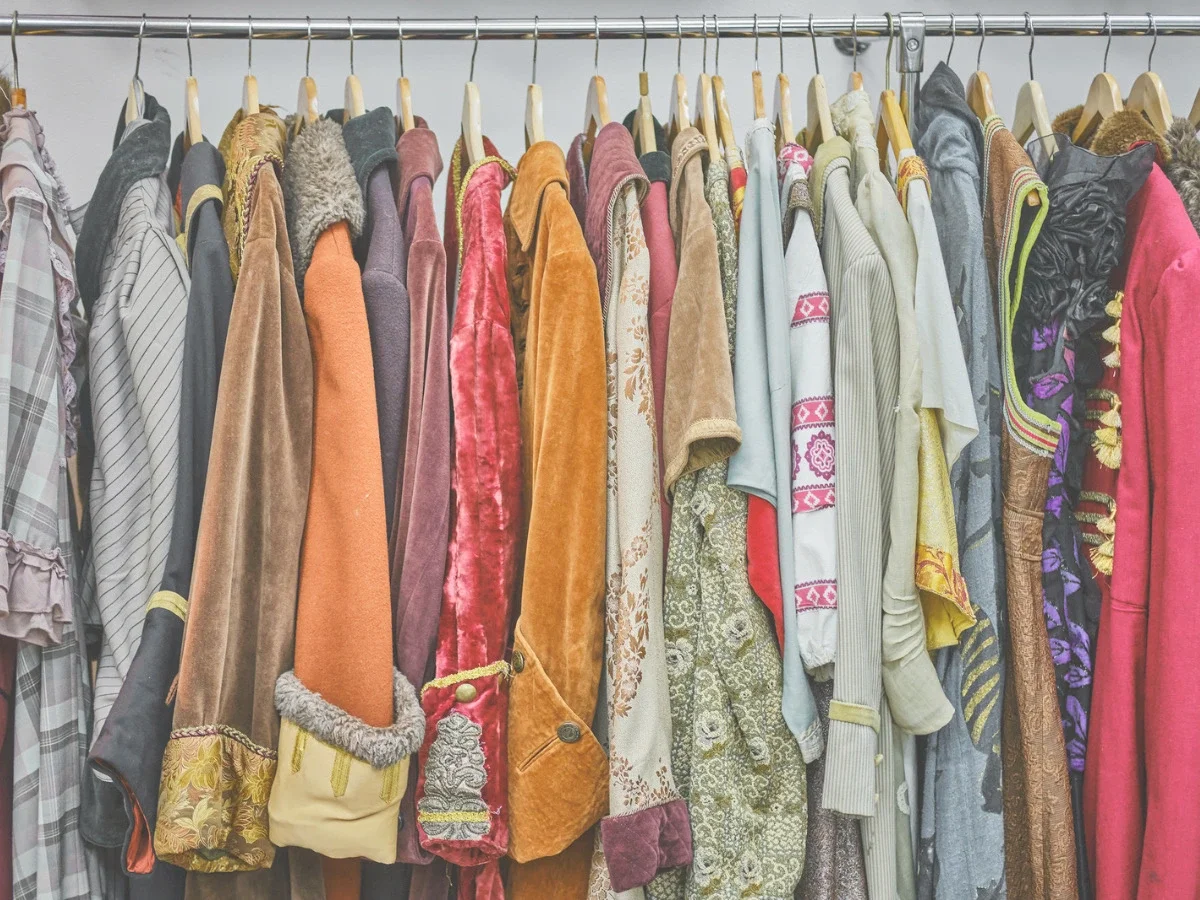 A tightly packed rack of richly colored and textured vintage garments in varied fabrics and patterns — accompanying "What Apfel Understood," the section of She The King's essay comparing Apfel to Schiaparelli, Westwood, and Chanel.