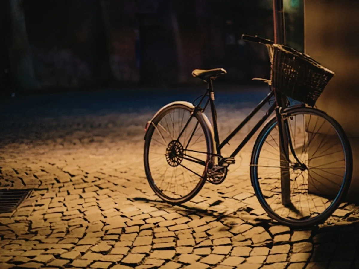 Vintage bicycle with a woven basket parked on a cobblestone street, lit by warm streetlight at night