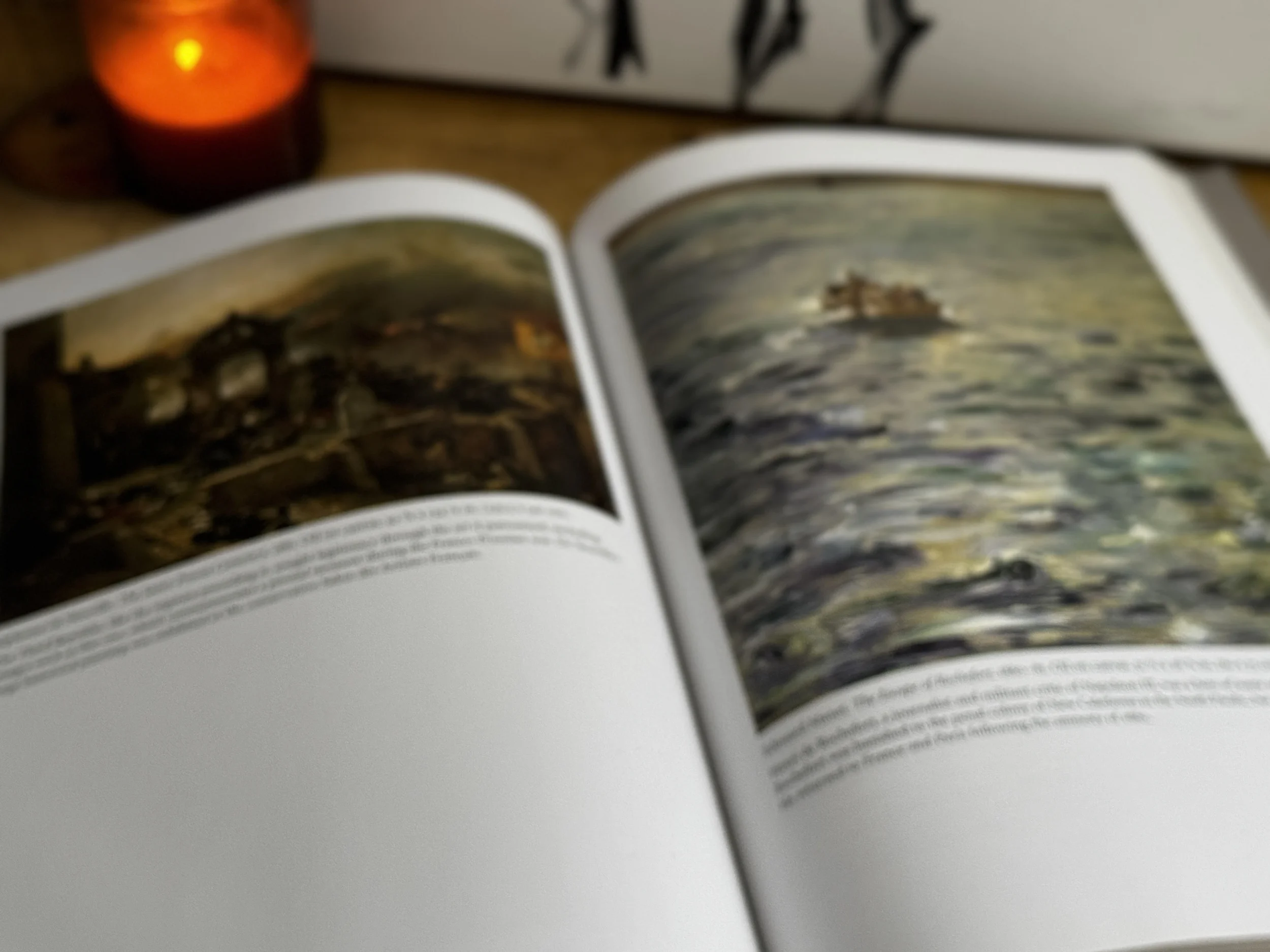 An open art book on a wooden surface with a lit candle glowing softly behind it — the solitary, intimate experience of turning to art in grief