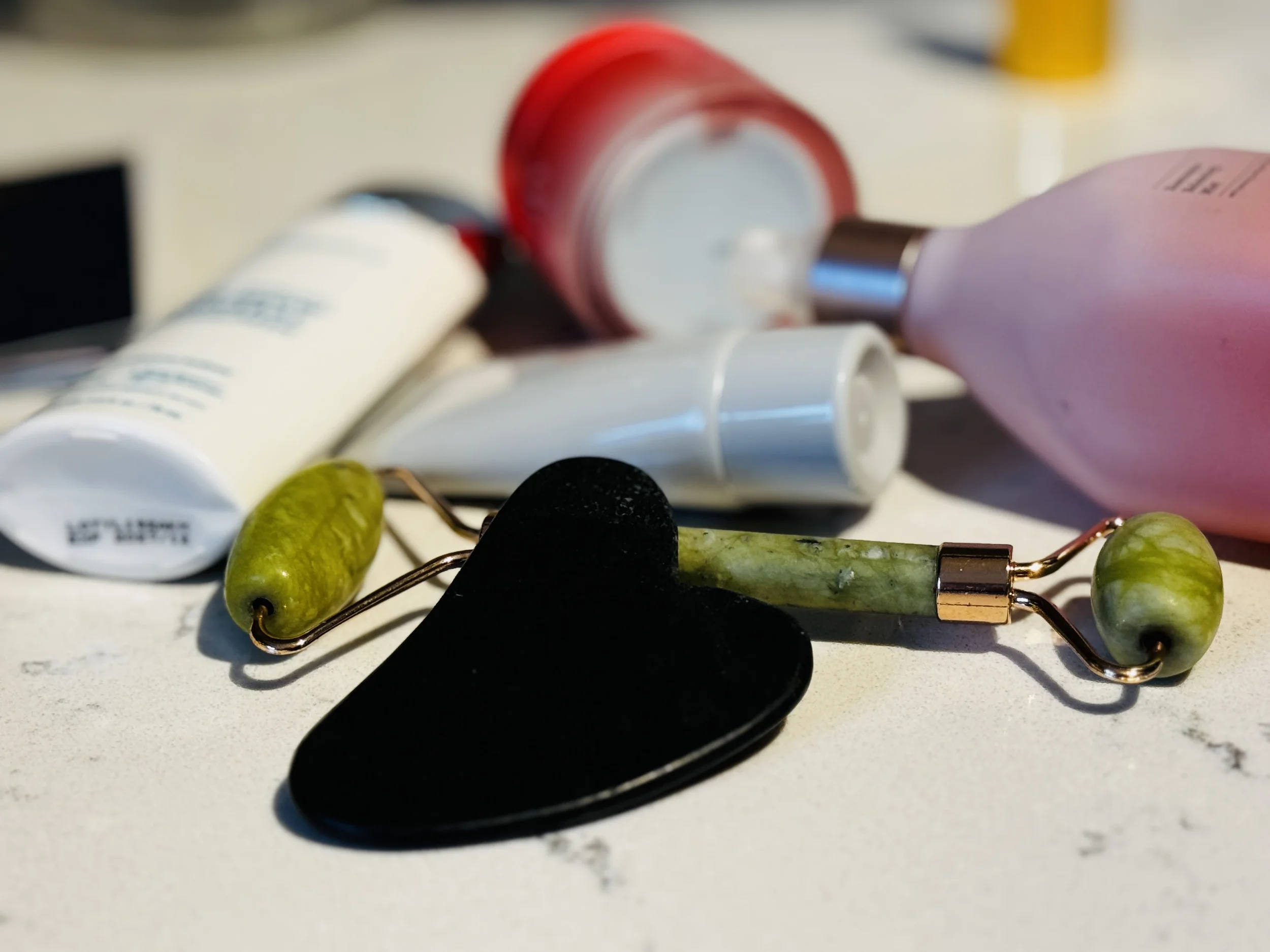 Gua sha stone and jade roller alongside travel skincare products on marble — optional non-toxic tools for reducing post-flight puffiness