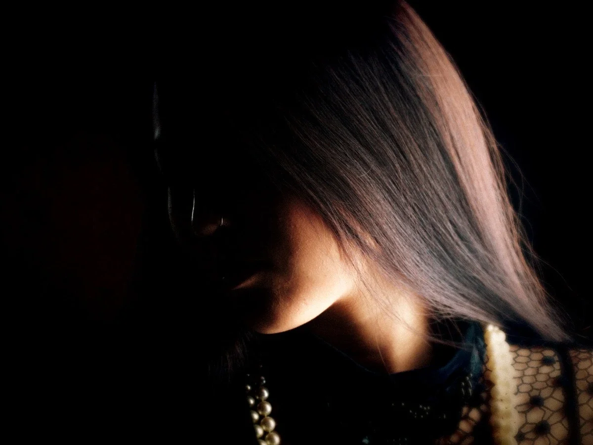 Partially obscured portrait of a woman in shadow examining visibility, concealment, and the performance of identity.