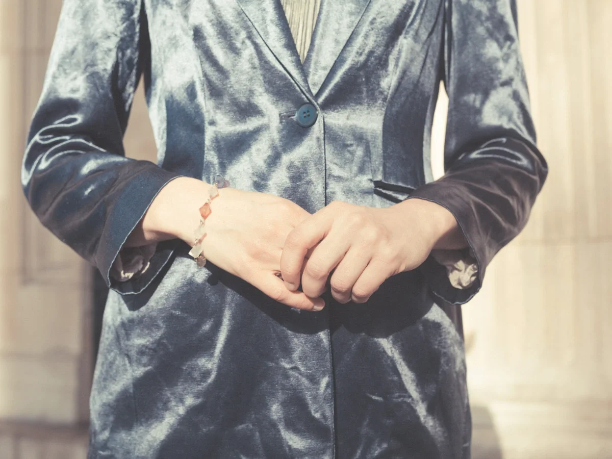 A woman seen from behind, hair in a loose bun, reaching for a garment on a closet rail — accompanying the opening section of She The King's Apfel essay on personal style and hesitation.