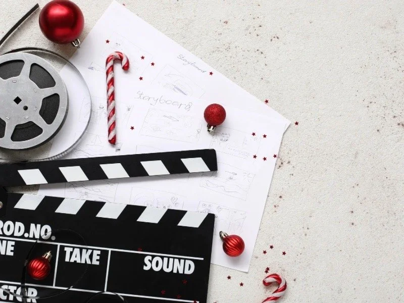 A film reel, storyboard sketches, clapperboard, and holiday decorations symbolizing classic and modern Christmas movies and festive filmmaking.