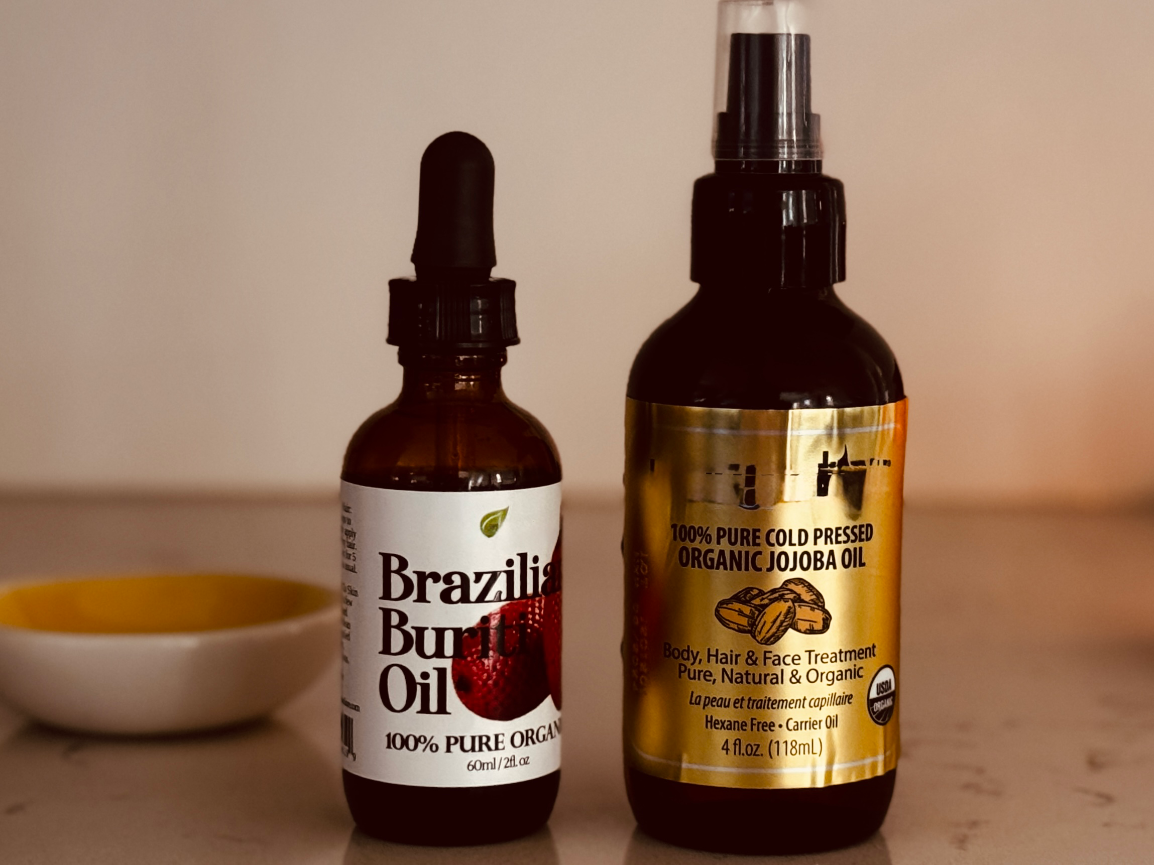Two bottles of organic hair treatment oils — Brazilian buriti oil and cold-pressed organic jojoba oil — used in a pre-shampoo hair barrier repair mask.