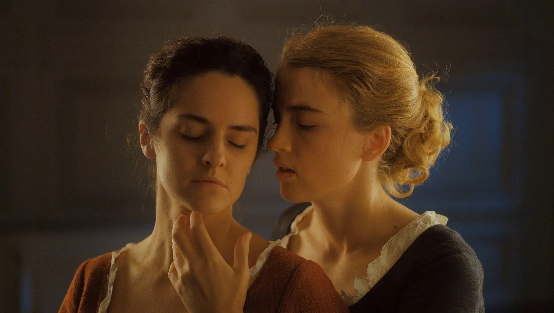 Two women stand in close proximity, one softly touching the other’s neck, portraying restrained desire shaped by religious pressure and internalized shame.