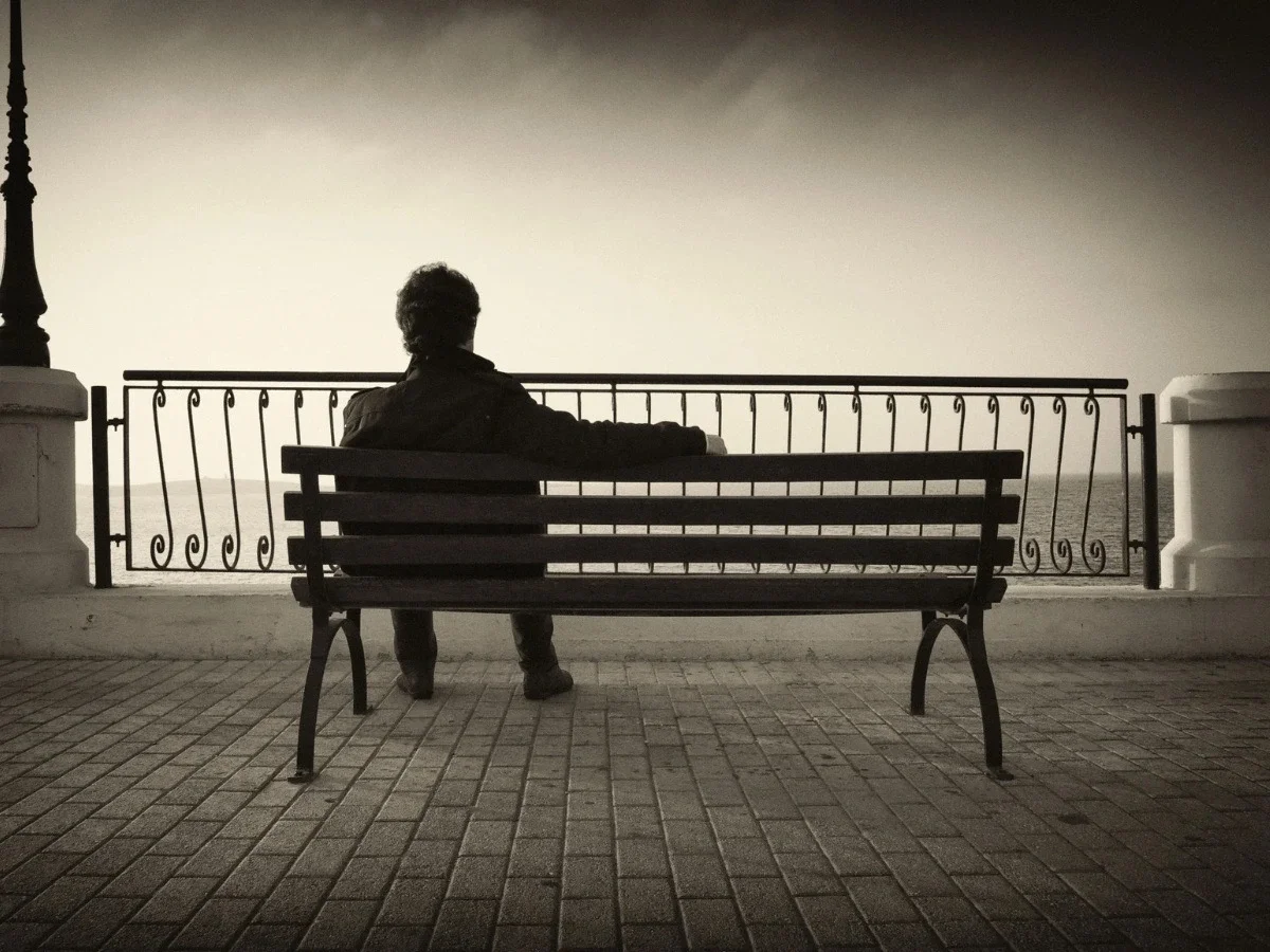 Person sitting alone on a bench facing the water, representing isolation, reflection, and emotional distance in queer cinema.