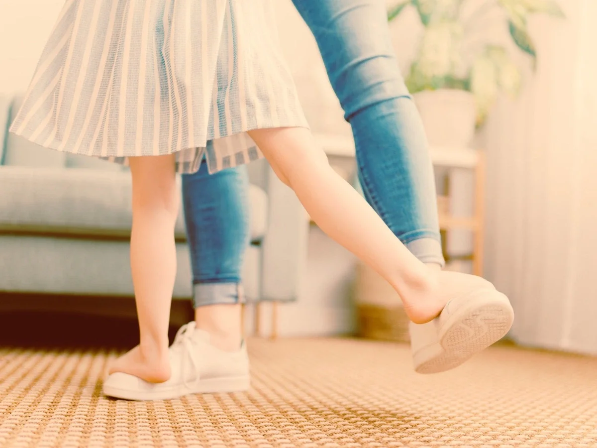 Close-up of a mother and child's feet mid-dance step in a living room