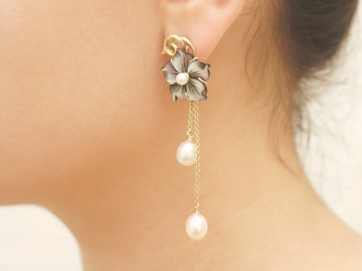 Close detail of a dramatic flower-and-pearl drop earring worn at the ear and neck, no face shown — accompanying "What Iris Apfel Knew About Getting Dressed," She The King's essay on personal style and self-editing.
