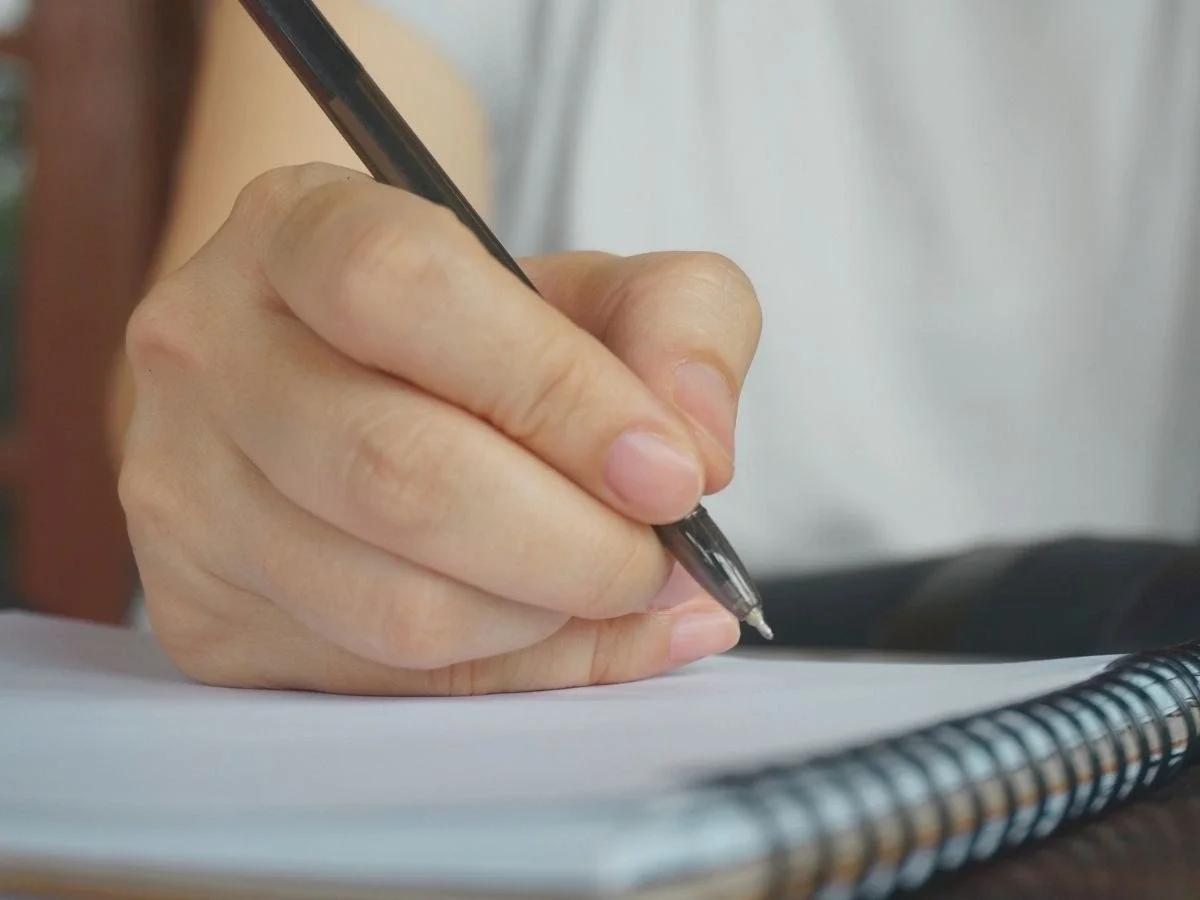 Close-up of a woman's hand writing in a notebook — representing the quiet, internal work of reclaiming your own emotional truth.