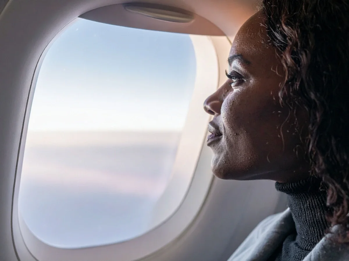 Woman gazing out airplane window in dry cabin air highlighting how flying causes skin dehydration