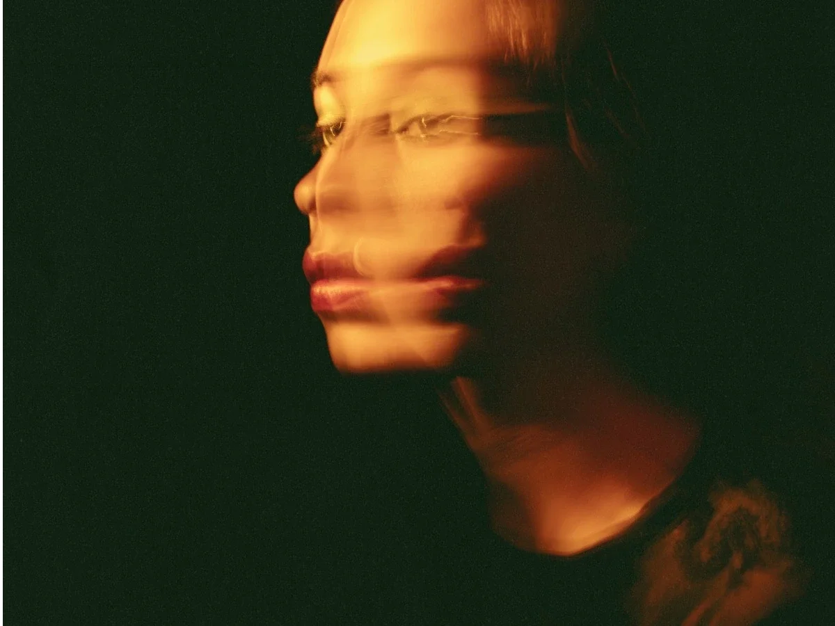 Blurred double-exposure portrait of a woman in warm light exploring identity, self-perception, and contemporary self-portraiture.