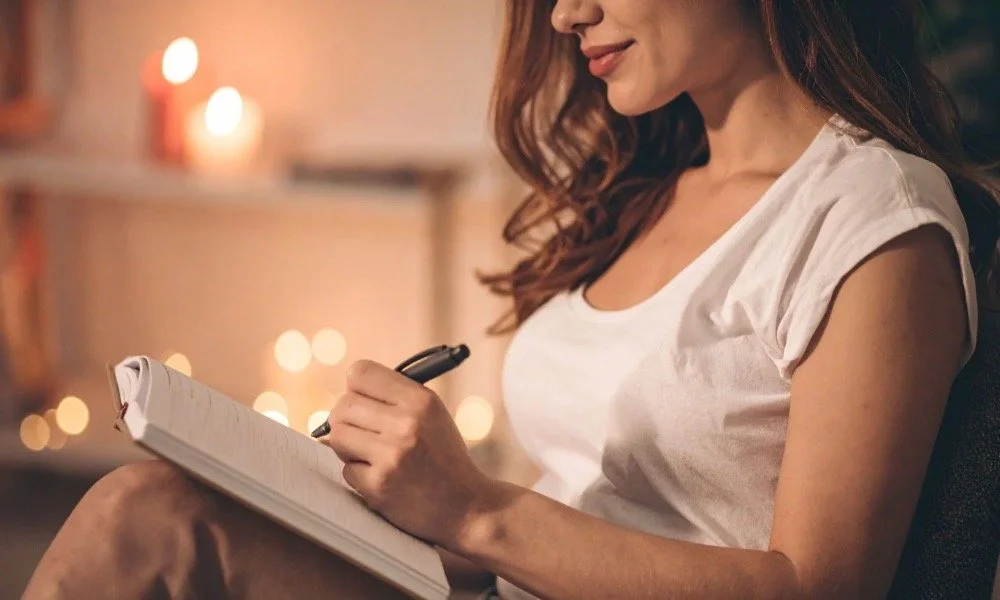Person writing in a journal in a cozy setting, representing daily self-care rituals that support emotional and mental well-being.