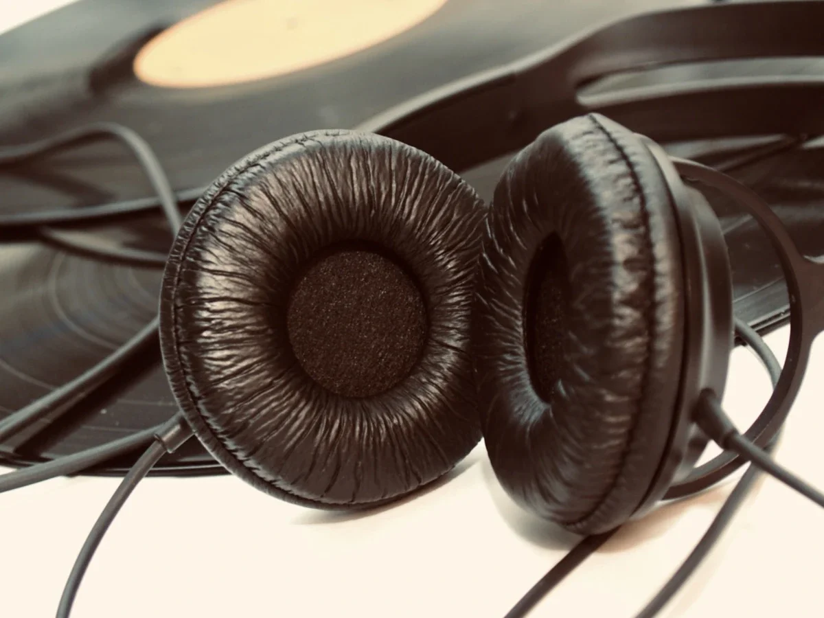 Wireless black headphones beside a LP and CD disks on red light, representing immersive listening and music as cultural travel.